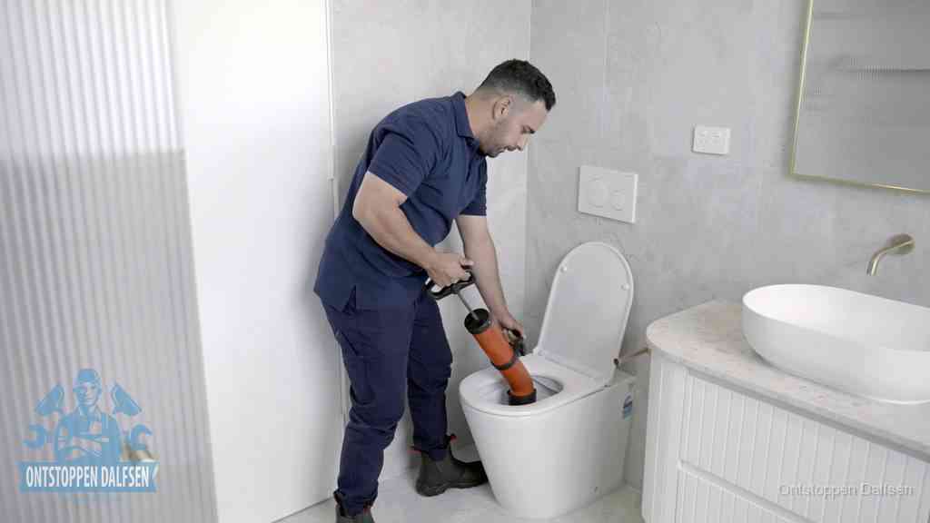 Een monteur buigt over een wandcloset en duwt met de hand een persluchtontstopper in de toiletpot om de verstopping handmatig los te maken in Dalfsen