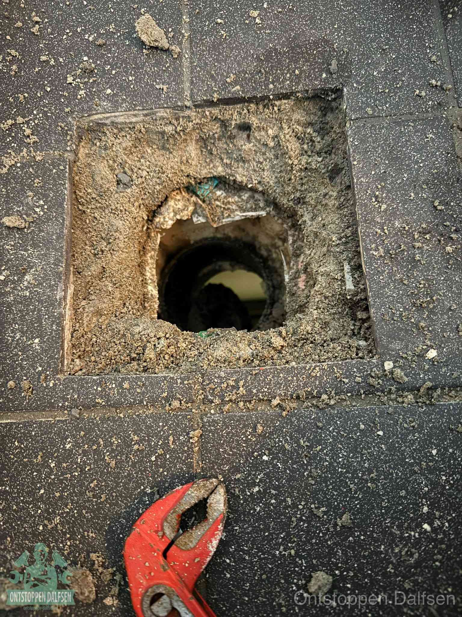 Een geopend rioolputje in een betontegelvloer met losgemaakt rooster en een zichtbare ronde afvoerbuis, het achterhalen waar de afvoerverstopping zit in Dalfsen
