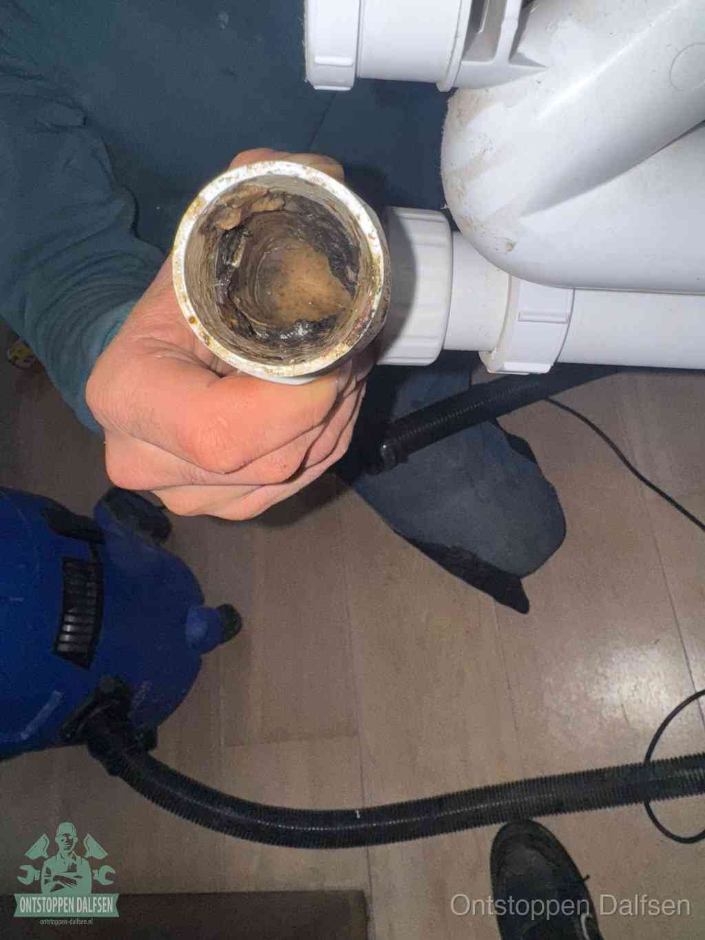 Een hand houdt een losgekoppeld PVC-afvoerbuisstuk vast dat van binnen volledig is dichtgeslibd met vet, vuil en aanslag, de meest voorkomende oorzaak van een verstopte afvoer in Dalfsen