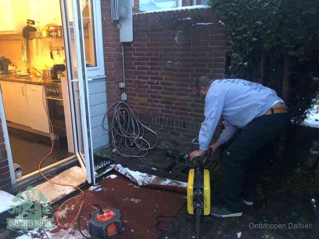 Een monteur werkt buiten bij een open riool-/grondput met een elektrische ontstoppingsmachine om een verborgen afvoerprobleem op te sporen in Dalfsen