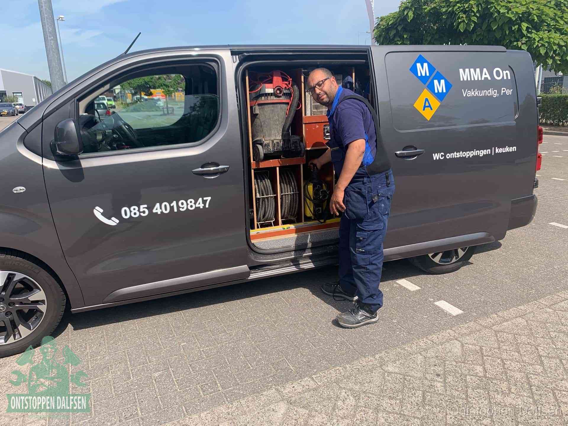 Een monteur bij de open schuifdeur van zijn bedrijfsbus op een parkeerplaats, klaar om de oorzaak van terugkerende afvoerverstoppingen aan te pakken in Dalfsen