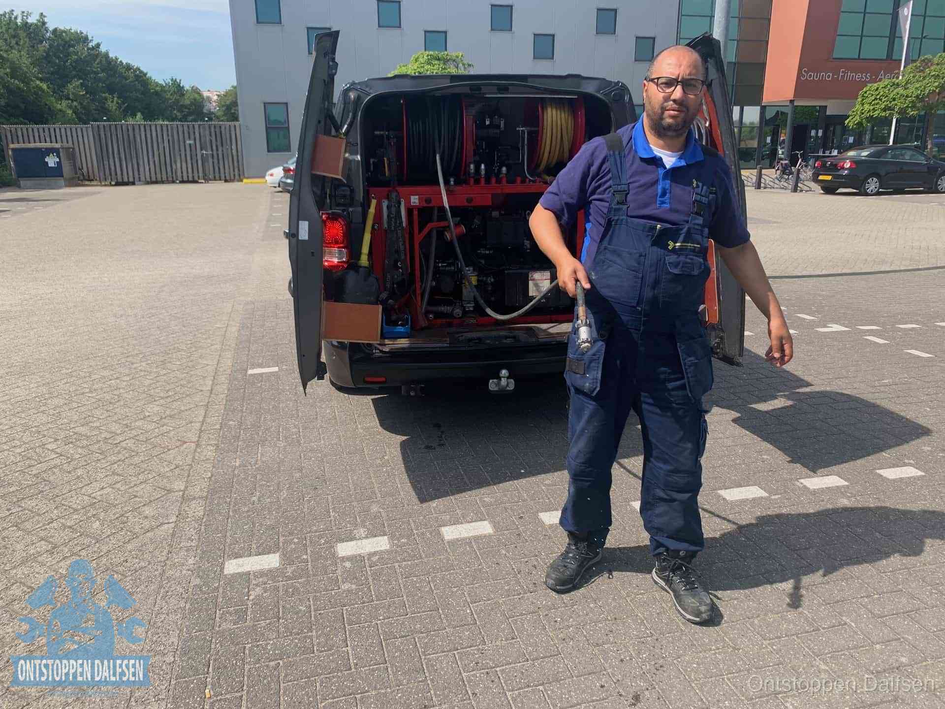 Een monteur bij zijn bestelbus met een hogedruk- en rioolreinigingsunit, klaar om de oorzaak van terugkerende wc-verstoppingen aan te pakken in Dalfsen