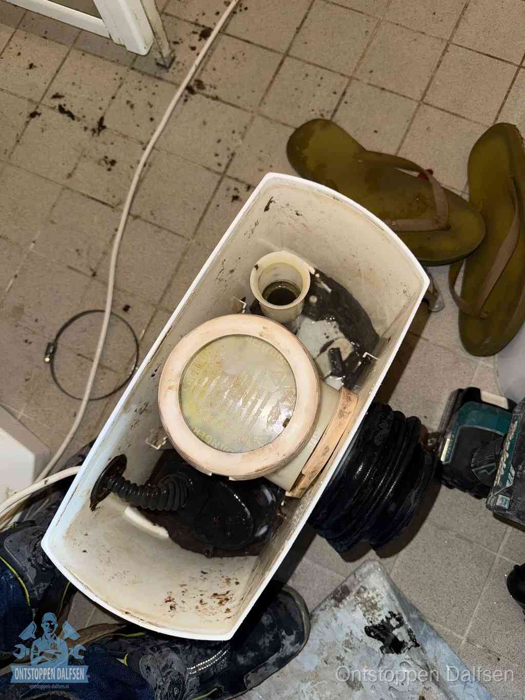 Een gedemonteerde toiletpot op de vloer met ontstoppingsveer en gereedschap ernaast, het verwijderen van een vastzittend voorwerp uit de wc in Dalfsen