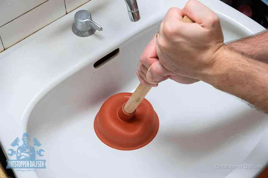 Twee handen gebruiken een rode rubberen plopper op een sanitair-afvoer om het toilet te ontstoppen in Dalfsen